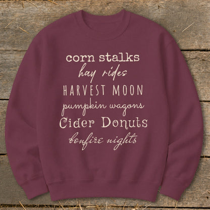 Maroon sweatshirt with white text listing "corn stalks, hay rides, HARVEST MOON, pumpkin wagons, Cider Donuts, bonfire nights".