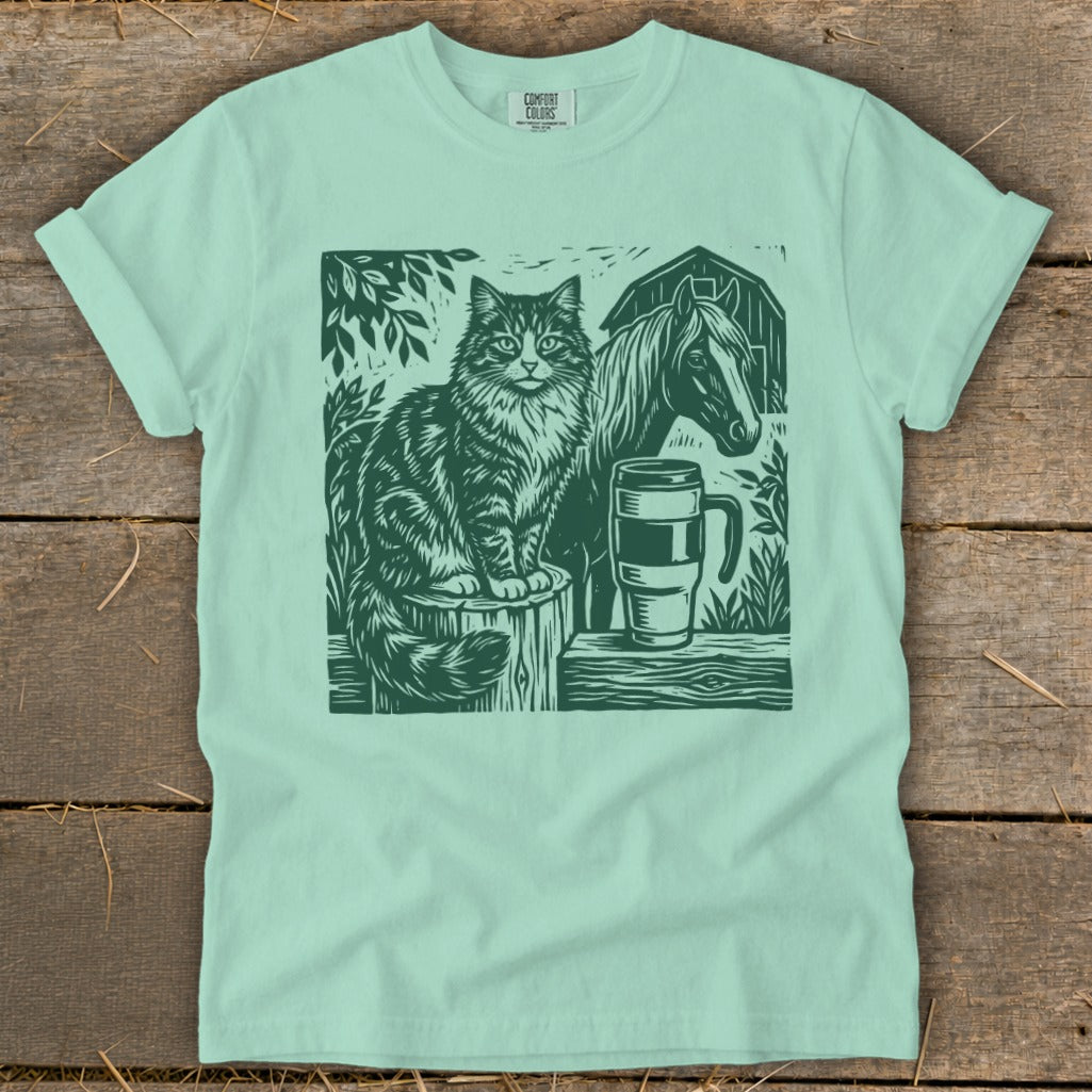 Green linocut of cat, horse, barn, and mug on a mint t-shirt.