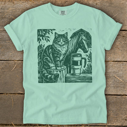 Green linocut of cat, horse, barn, and mug on a mint t-shirt.