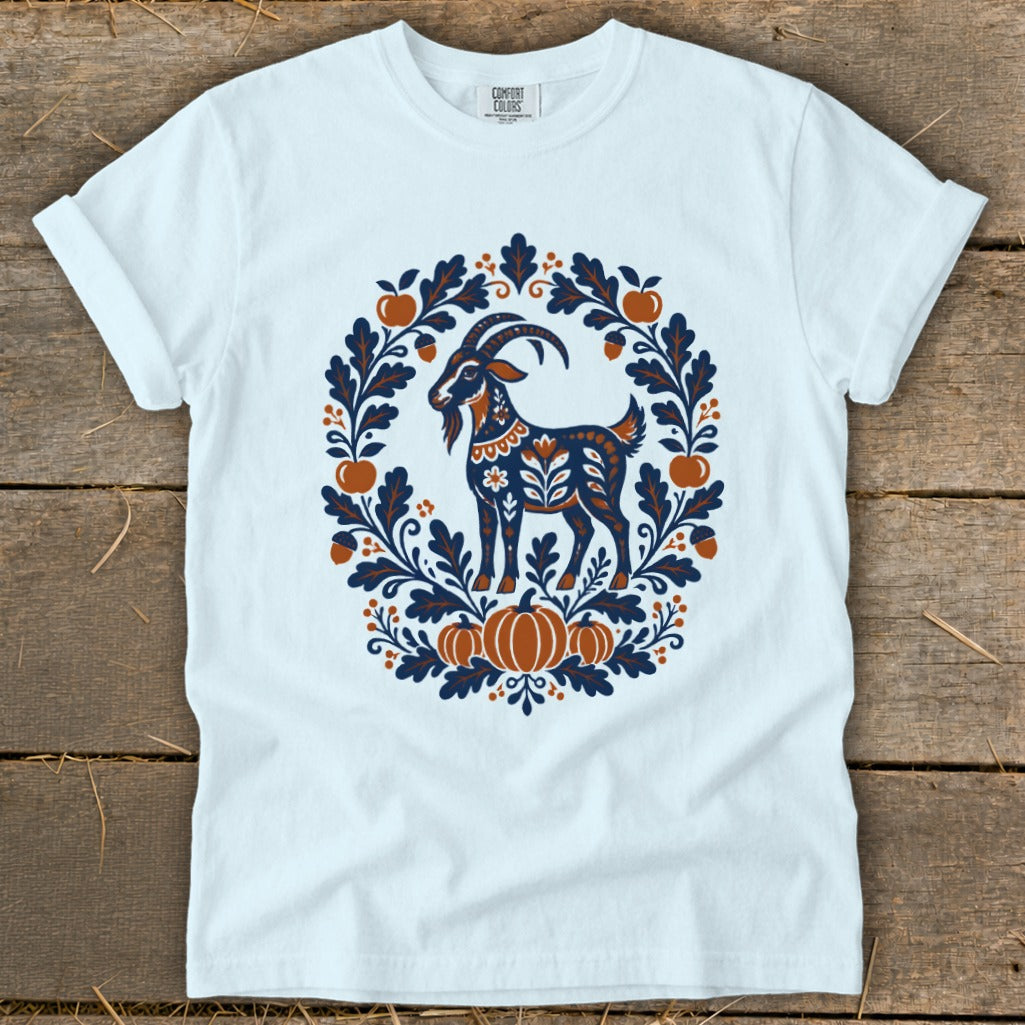 A light blue t-shirt with a folk-art graphic of a goat surrounded by leaves and pumpkins.