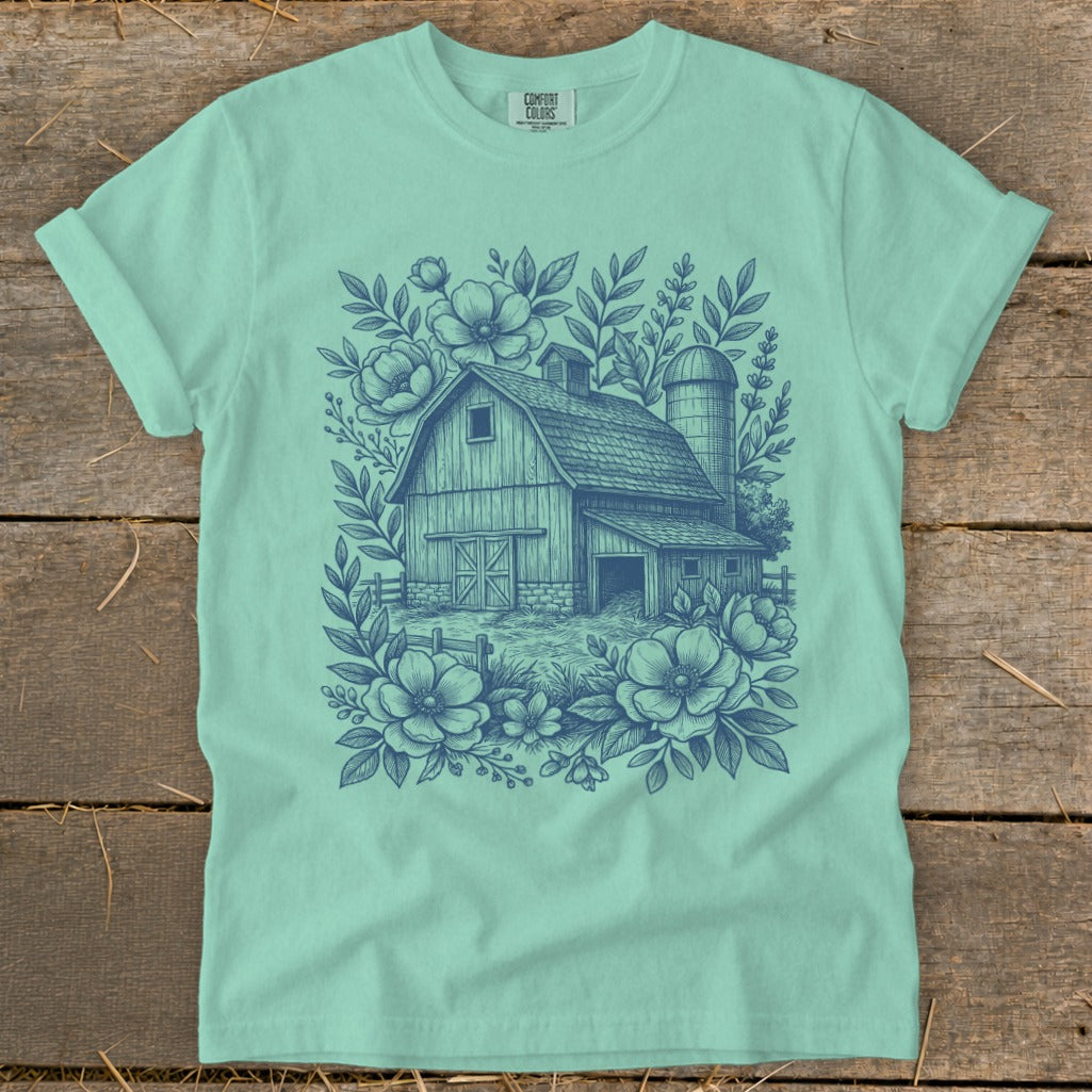 Teal t-shirt with a blue line drawing of a barn, silo, fence, and flowers.