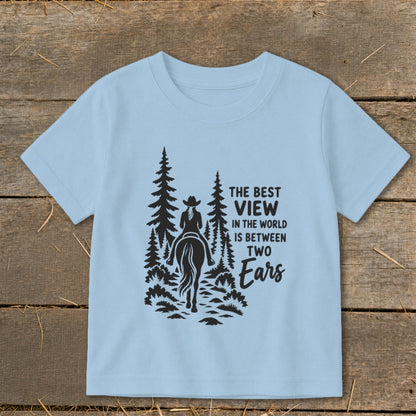 Light blue t-shirt featuring a silhouette of a person on a horse riding through trees with text reading, The best view in the world is between two ears.