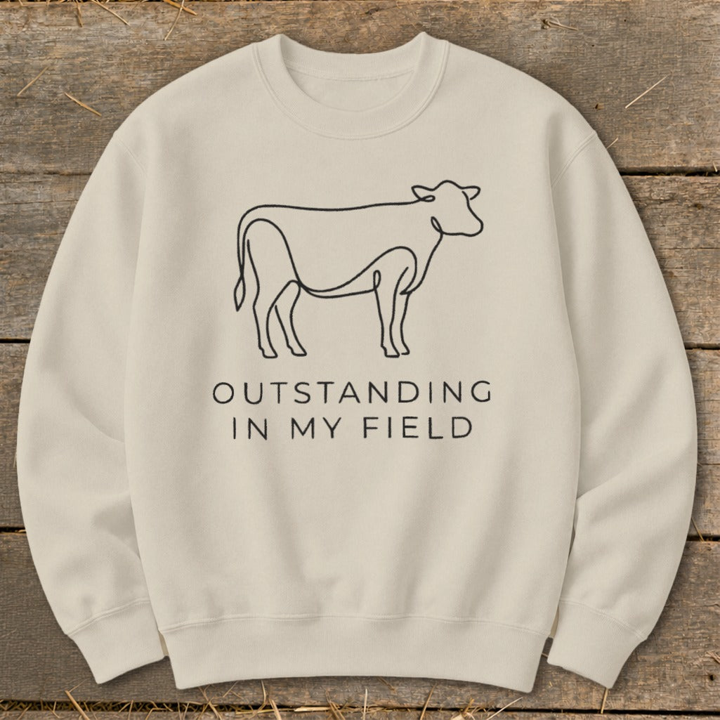 Cream sweatshirt with line drawing of a cow and text "OUTSTANDING IN MY FIELD".