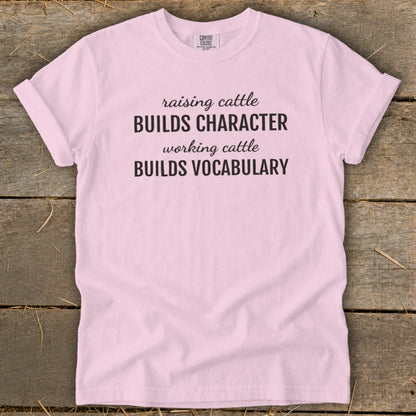 Pink t-shirt with black text: "raising cattle BUILDS CHARACTER working cattle BUILDS VOCABULARY".