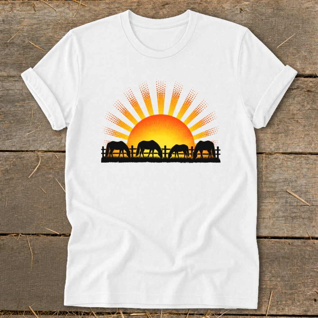White t-shirt with a graphic of horses grazing in front of a rising sun.