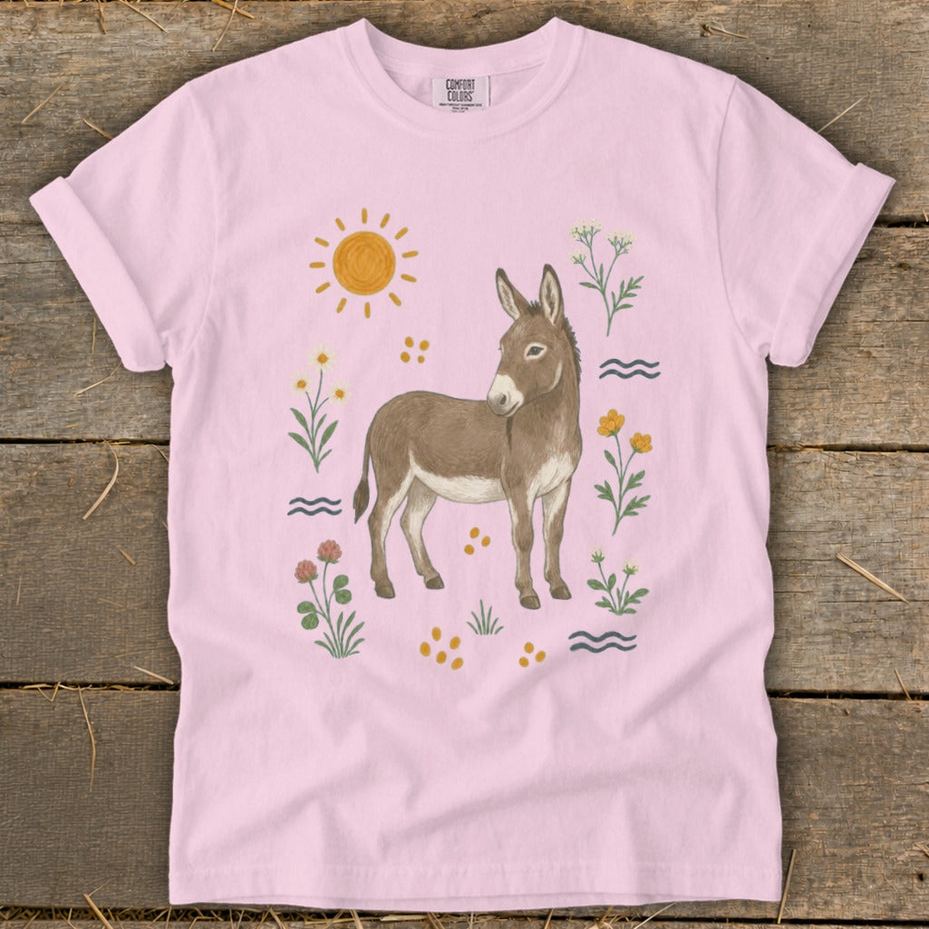 Pink t-shirt with watercolor illustration of a donkey surrounded by flowers and a sun.