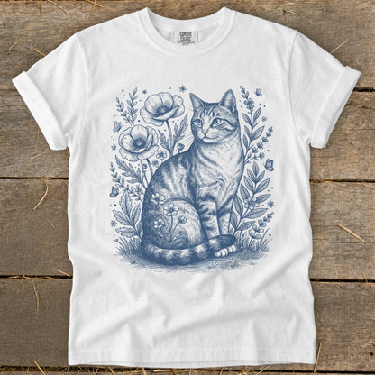 White t-shirt with a blue ink drawing of a tabby cat among wildflowers and butterflies.