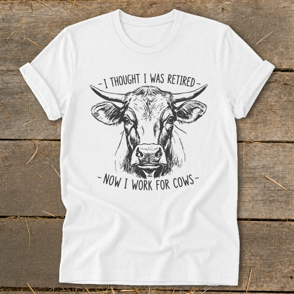 White t-shirt with black line art of a cow and text saying "I thought I was retired - Now I work for cows."