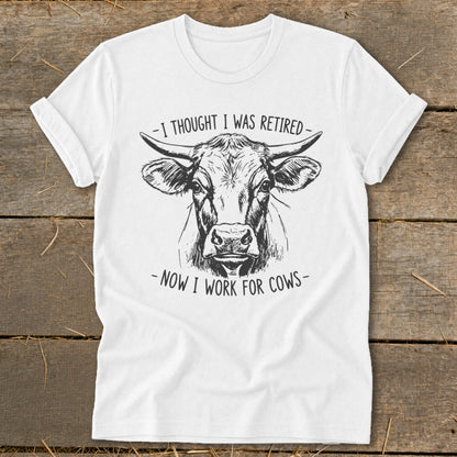 White t-shirt with black line art of a cow and text saying "I thought I was retired - Now I work for cows."