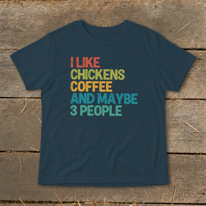 A dark blue t-shirt with retro multicolored text reading "I LIKE CHICKENS COFFEE AND MAYBE 3 PEOPLE."