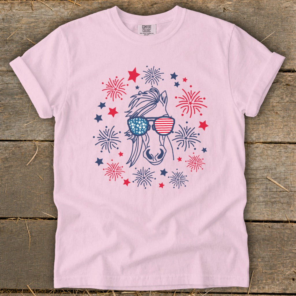 Pink t-shirt with a horse wearing American flag sunglasses surrounded by fireworks and stars.