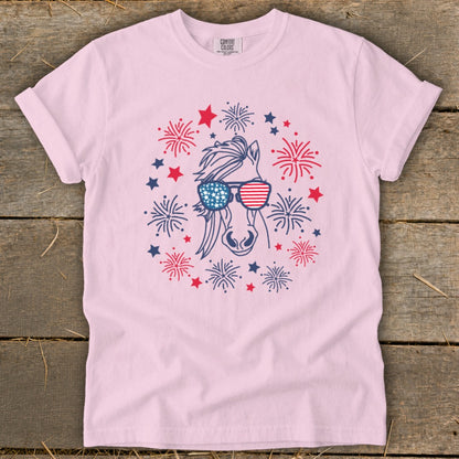 Pink t-shirt with a horse wearing American flag sunglasses surrounded by fireworks and stars.