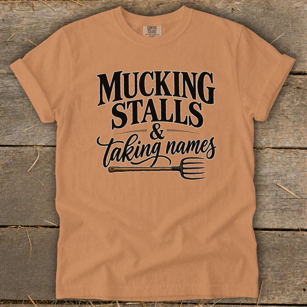 Peach t-shirt with "Mucking Stalls & Taking Names" text and pitchfork graphic.