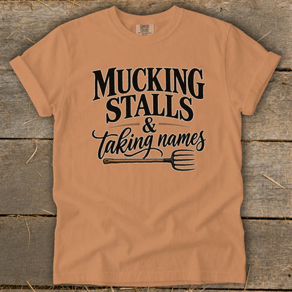 Peach t-shirt with "Mucking Stalls & Taking Names" text and pitchfork graphic.