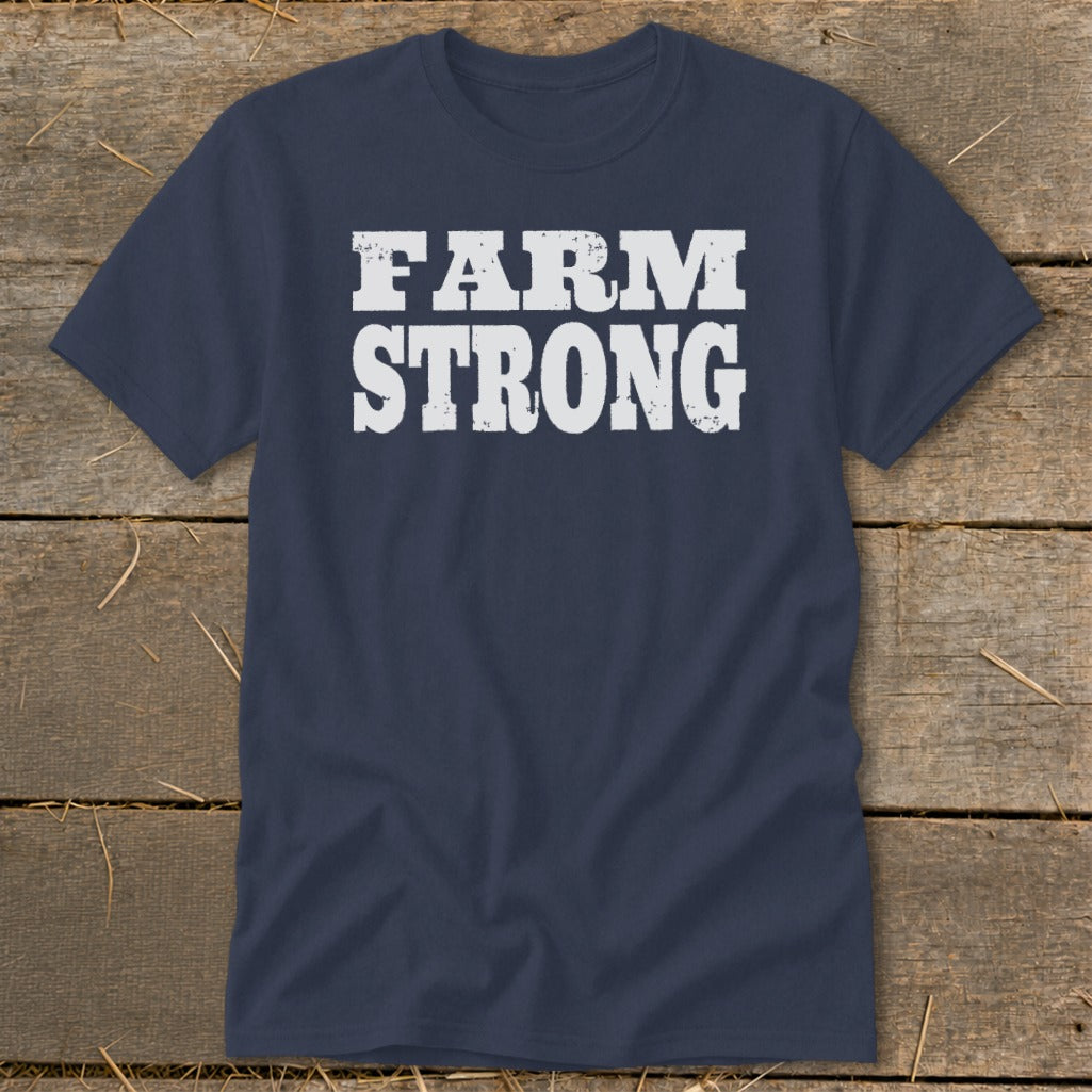 A dark blue t-shirt printed with the white distressed text FARM STRONG rests on wooden planks.