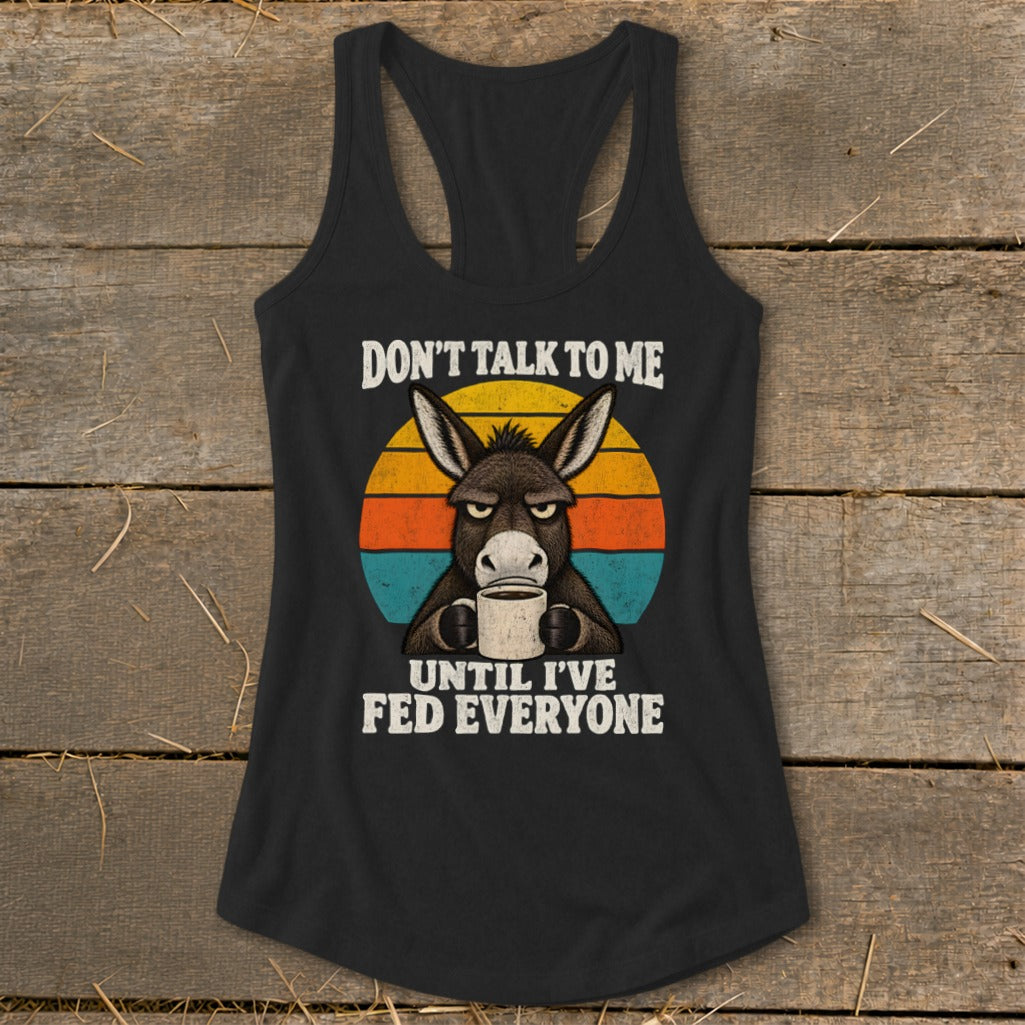 A black racerback tank top featuring a graphic of a grump donkey drinking coffee against a retro sunset, with the text DON'T TALK TO ME UNTIL I'VE FED EVERYONE.