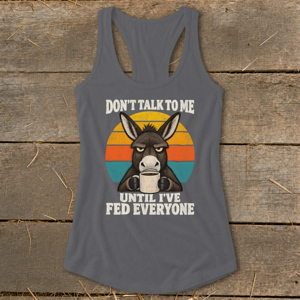 Dark gray women's racerback tank top featuring a grumpy donkey drinking coffee and text reading "Don't Talk to Me Until I've Fed Everyone."