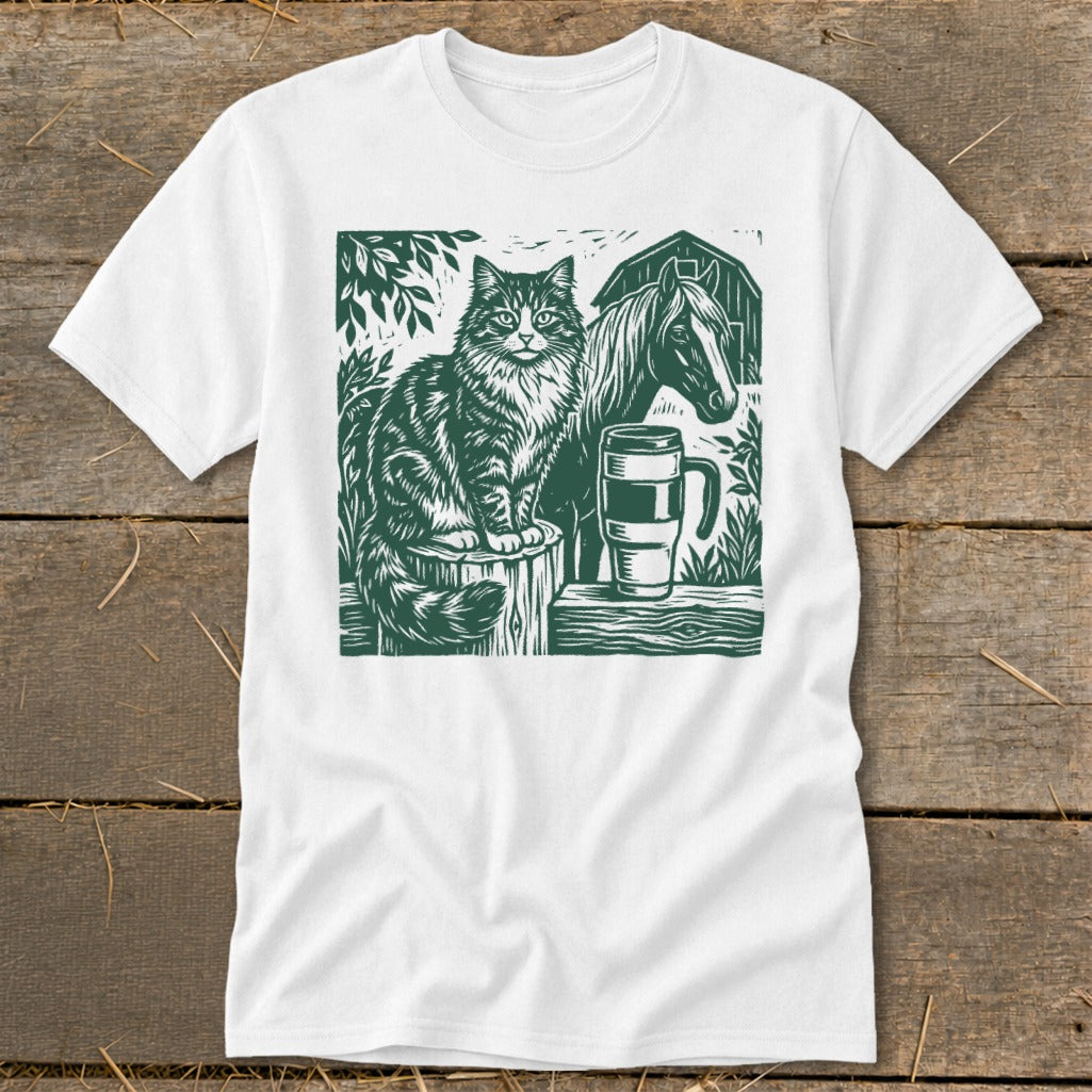 Green linocut print of a cat, horse, barn, and mug on a white t-shirt.