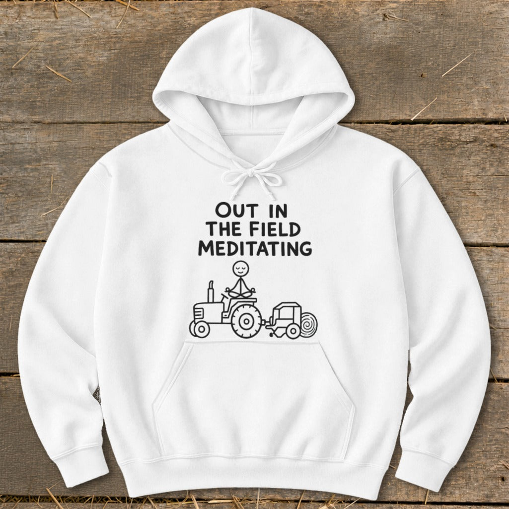 White hoodie with "OUT IN THE FIELD MEDITATING" text and a stick figure meditating on a tractor.