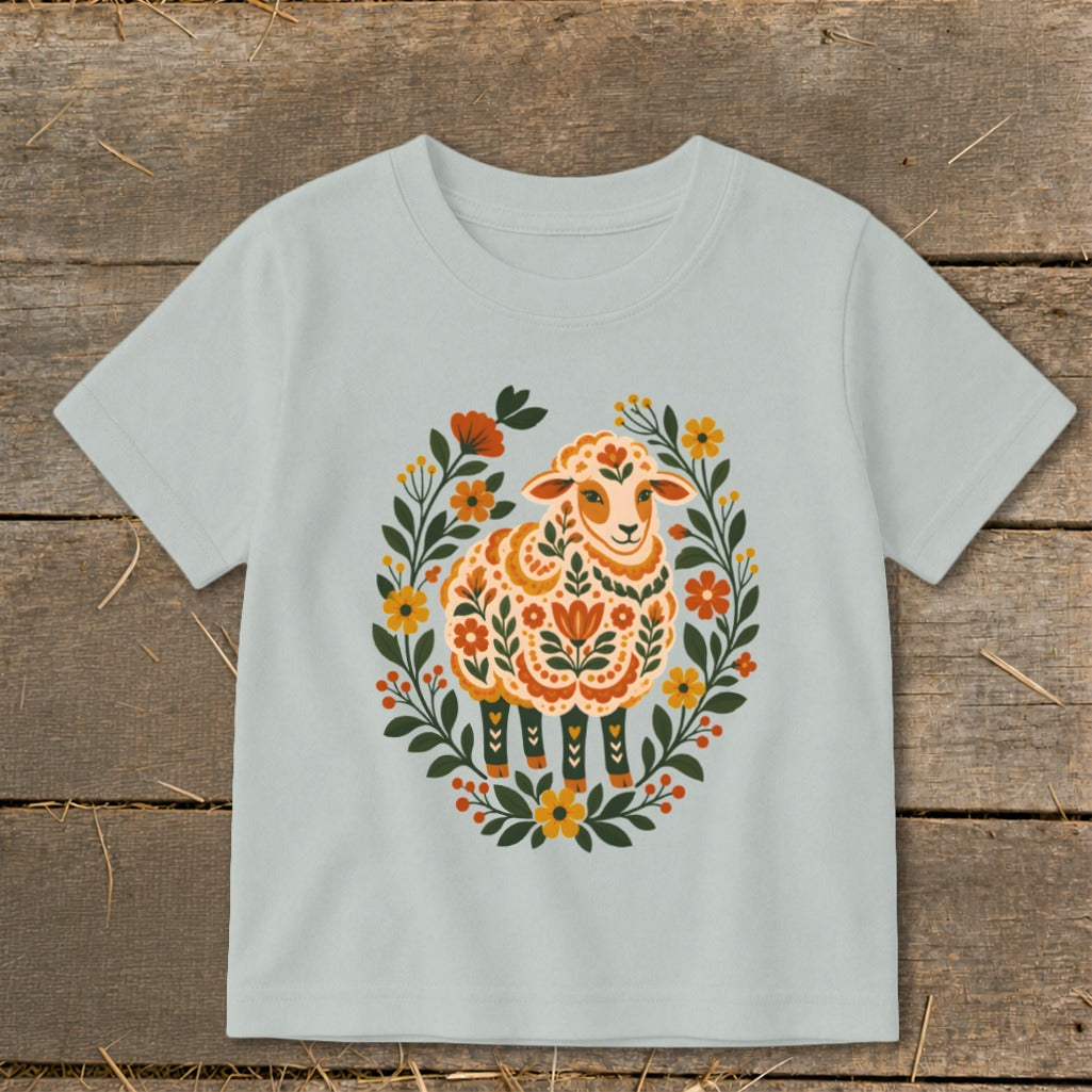 Light blue t-shirt with a decorative folk art sheep surrounded by a floral wreath.