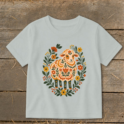 Light blue t-shirt with a decorative folk art sheep surrounded by a floral wreath.
