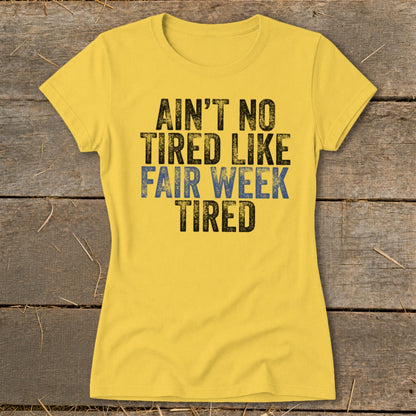 Yellow t-shirt with distressed text reading "AIN'T NO TIRED LIKE FAIR WEEK TIRED".
