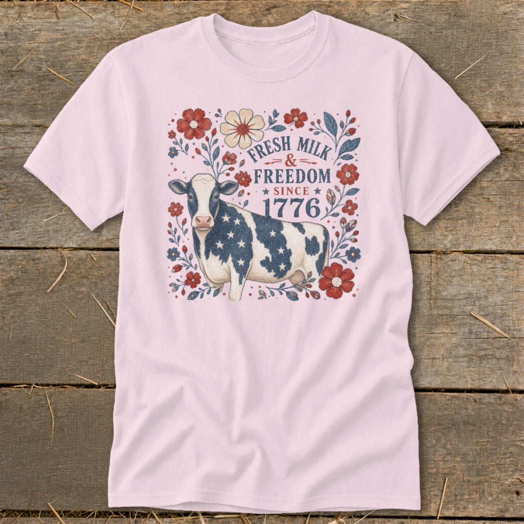 Pink t-shirt with a cow decorated in stars and stripes, surrounded by flowers, with text "Fresh Milk & Freedom Since 1776".