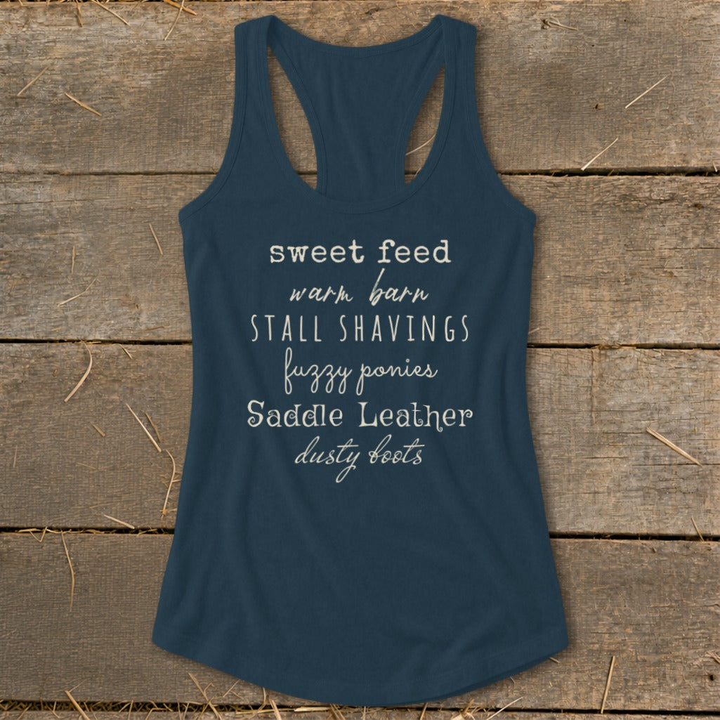 Navy tank top with white text listing equestrian items: sweet feed, warm barn, stall shavings, fuzzy ponies, saddle leather, dusty boots.