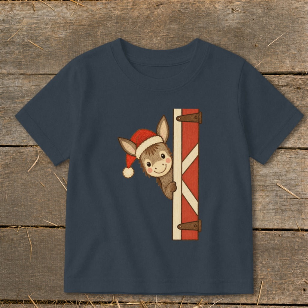 Donkey wearing Santa hat peeking from behind barn door on navy t-shirt.
