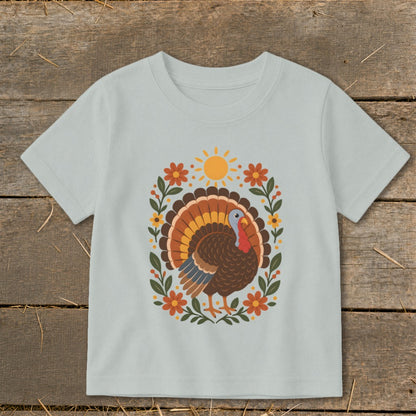 Light blue t-shirt with a Thanksgiving turkey graphic surrounded by flowers and a sun.