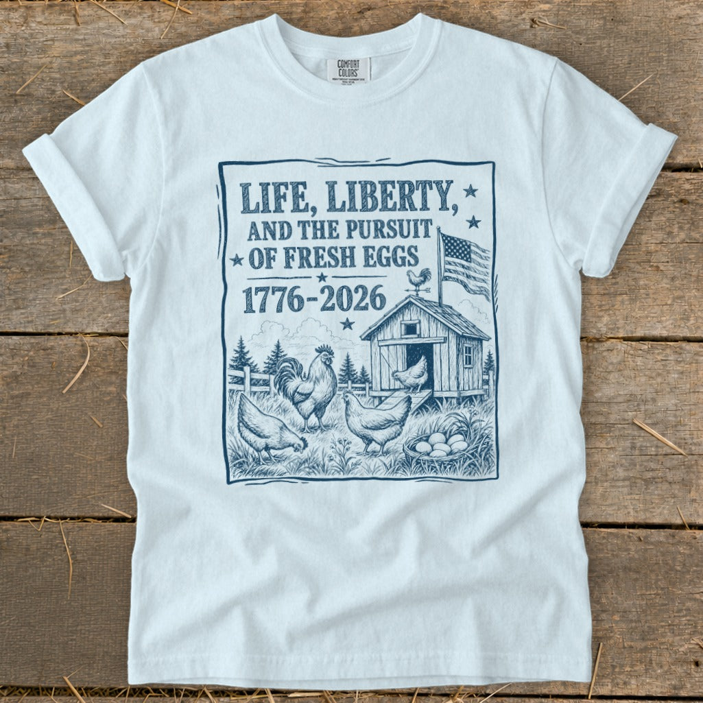 White t-shirt with blue graphic: LIFE, LIBERTY, AND THE PURSUIT OF FRESH EGGS 1776-2026