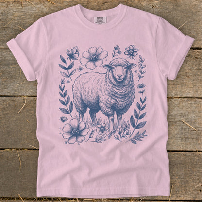 Pink t-shirt with a blue sketch of a sheep surrounded by flowers.
