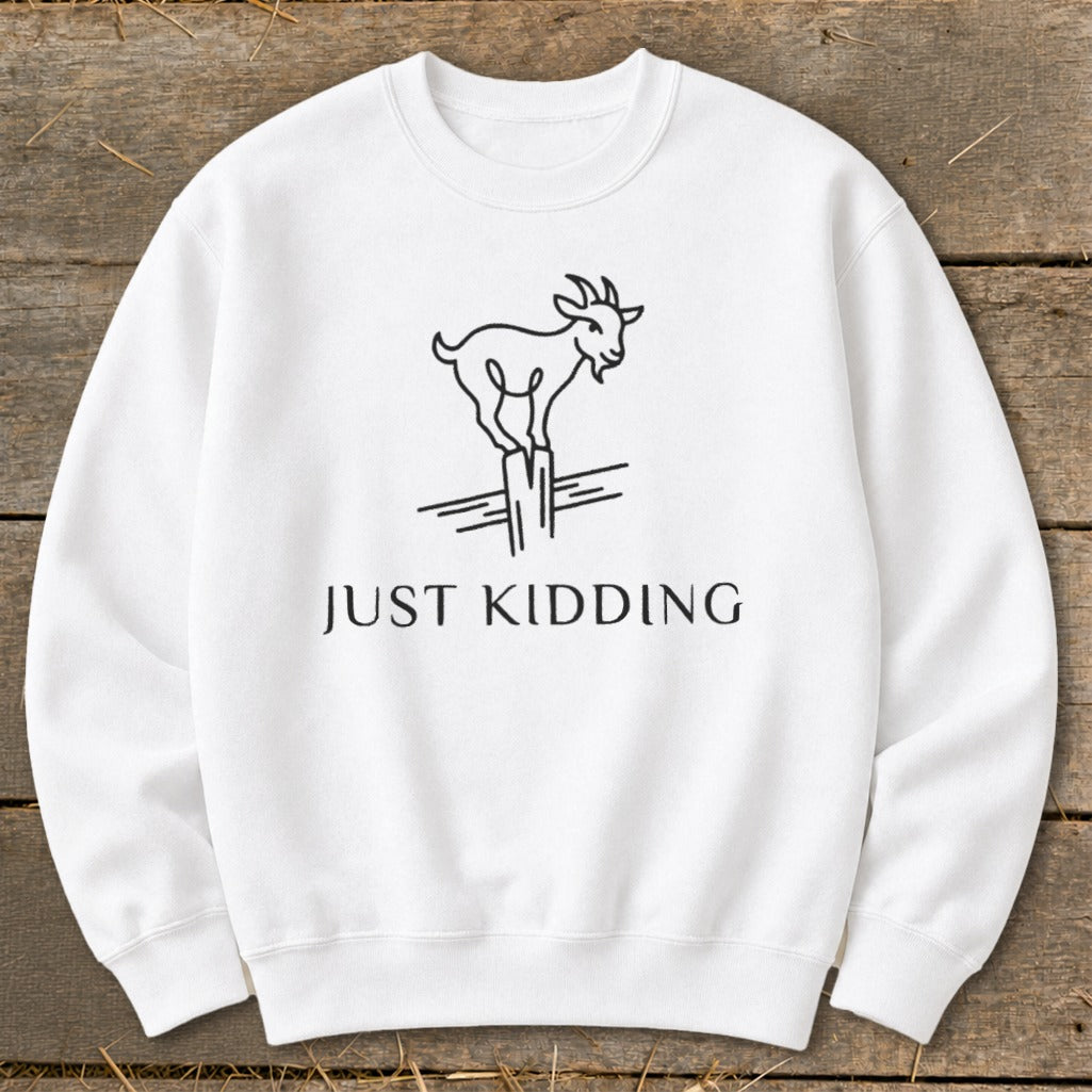 White sweatshirt with a line drawing of a goat standing on a post and the text "JUST KIDDING".