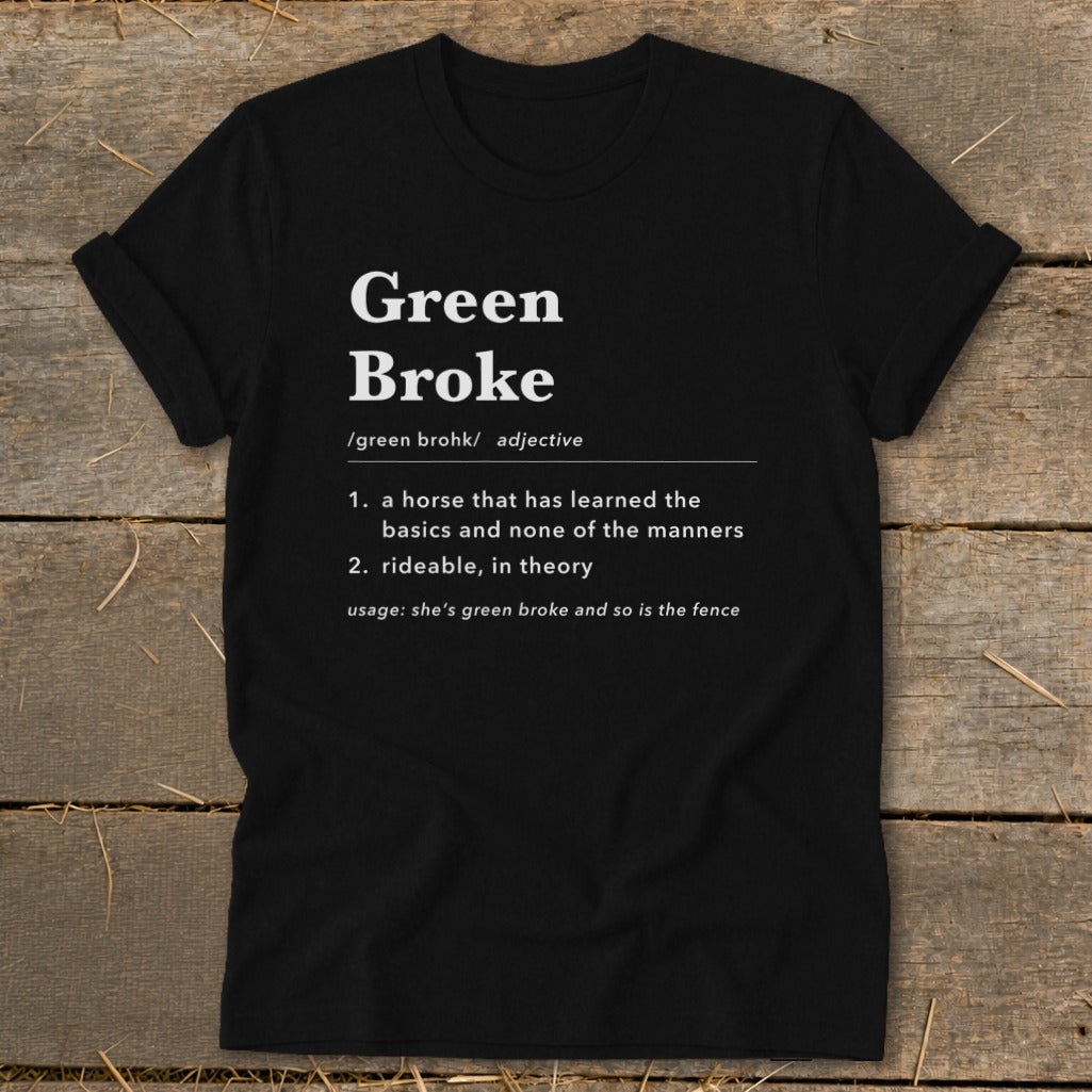 Black t-shirt featuring dictionary-style text defining the term green broke laid flat on a rustic wooden surface.