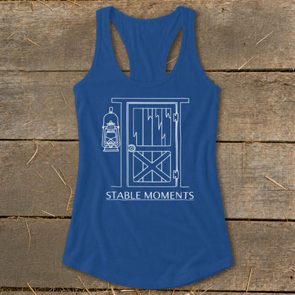 Blue racerback tank top with white barn door and lantern graphic and "STABLE MOMENTS" text.