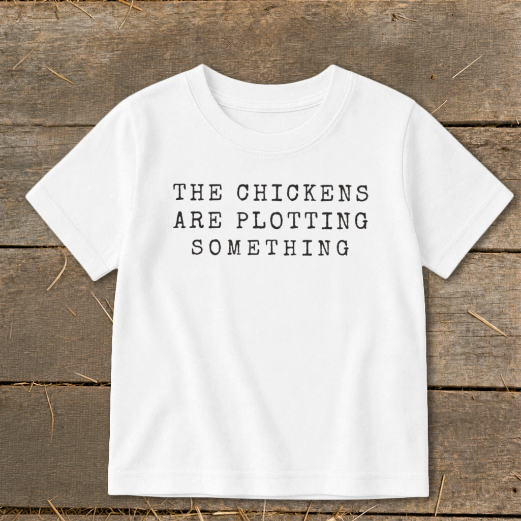 White t-shirt with black text that reads "THE CHICKENS ARE PLOTTING SOMETHING".