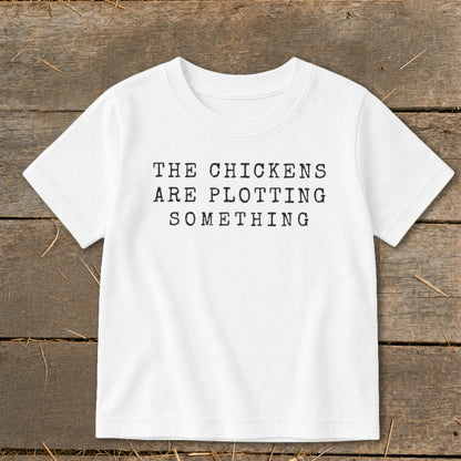White t-shirt with black text that reads "THE CHICKENS ARE PLOTTING SOMETHING".