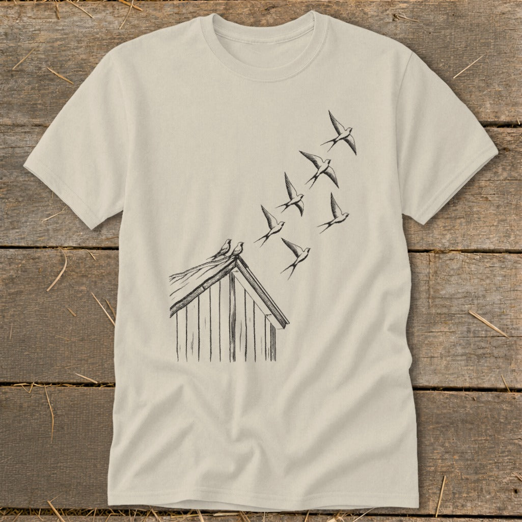 Light beige t-shirt featuring a line drawing of a small shed with birds flying upward from the roof.