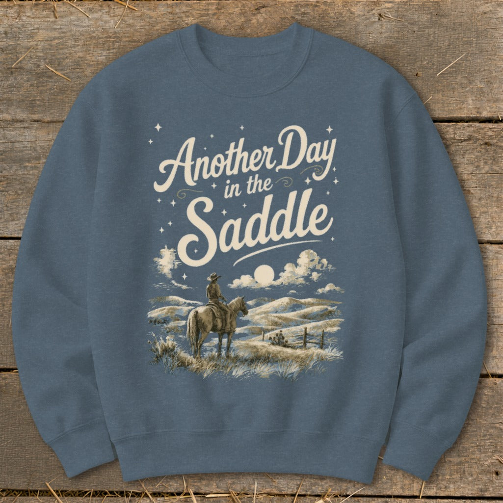 Crewneck sweatshirt with "Another Day in the Saddle" text over cowboy on horseback in a landscape.