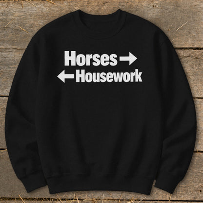 A black crewneck sweatshirt with white text reading Horses with a right arrow and Housework with a left arrow.