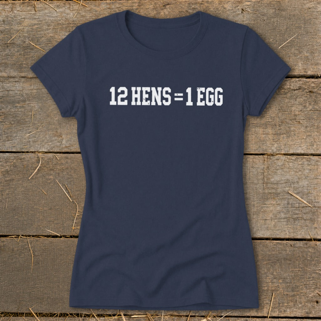 Navy blue women's t-shirt featuring the white distressed text 12 HENS = 1 EGG, laid flat on rustic wood.