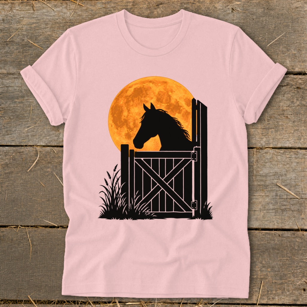 A light pink t-shirt displays a graphic of a horse looking out a stable door against an orange moon.