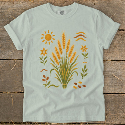 Light blue t-shirt with wheat stalks, sun, flowers, leaves, and seeds graphic.