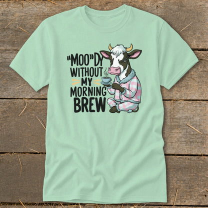 Light green t-shirt with a cow in pajamas holding coffee and text "Moo"dy Without My Morning Brew.