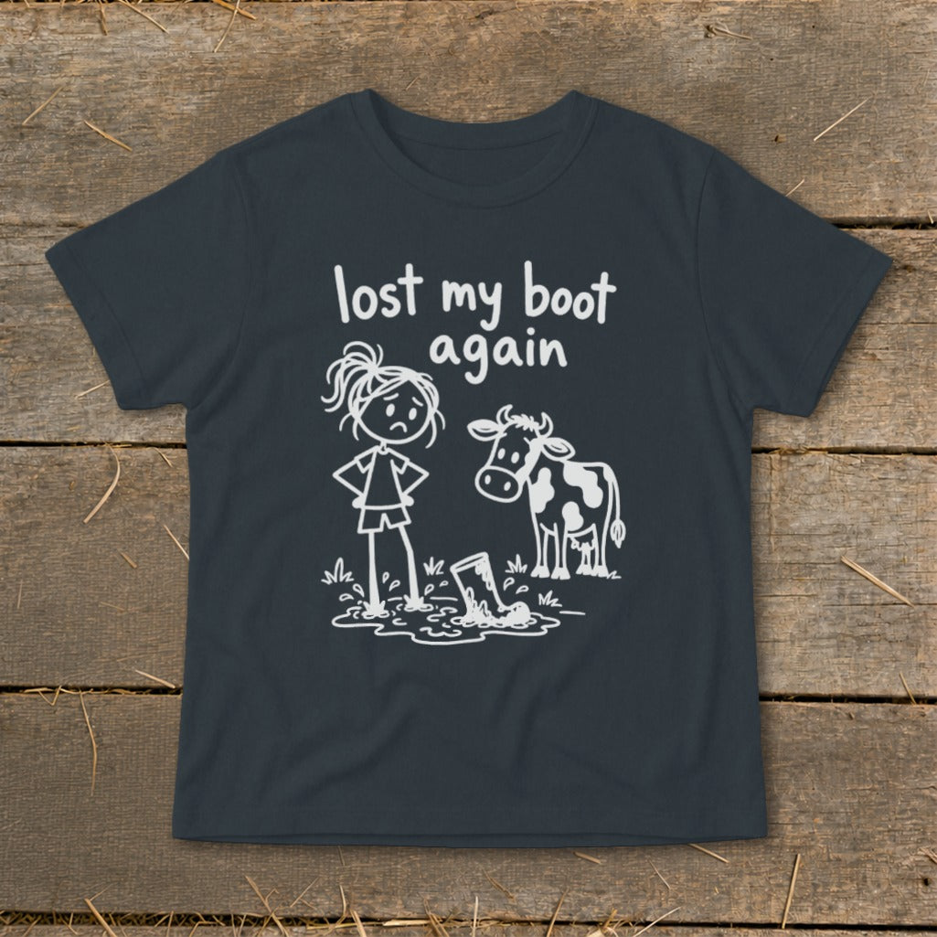 A dark grey t-shirt featuring a white graphic of a frustrated stick-figure girl and a cow looking at a boot stuck in mud, with the text "lost my boot again."