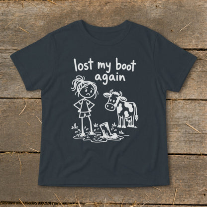 A dark grey t-shirt featuring a white graphic of a frustrated stick-figure girl and a cow looking at a boot stuck in mud, with the text "lost my boot again."