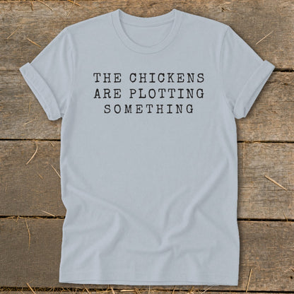 Light blue t-shirt with black text that reads "THE CHICKENS ARE PLOTTING SOMETHING".