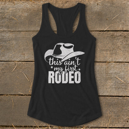 Black racerback tank top with white cowboy hat graphic and text: "this ain't my first RODEO".