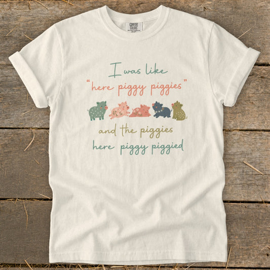 White t-shirt with text "I was like 'here piggy piggies' and the piggies here piggy piggied" and stylized pigs.