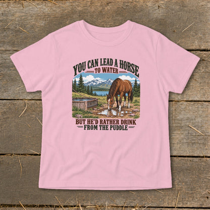 A pink t-shirt featuring a graphic of a horse drinking from a puddle with mountains behind it.